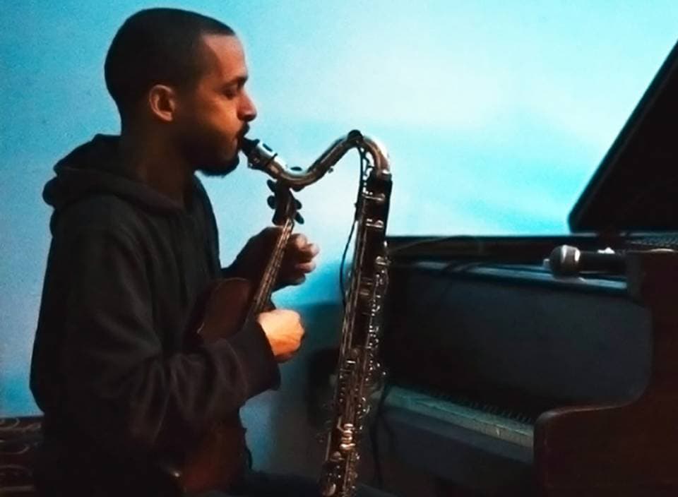 Yoni Silver plays a wind instrument and holds a violin near a piano.